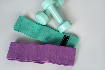  accessories such as turquoise dumbbells and rubber bands for sports isolated on white floor.