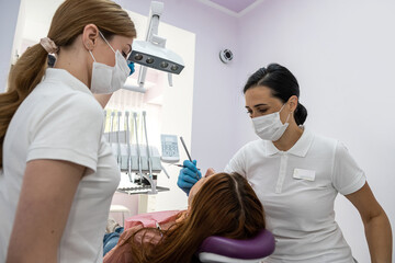 female dentist with a female assistant diagnoses and treats the teeth of a new girl patient.