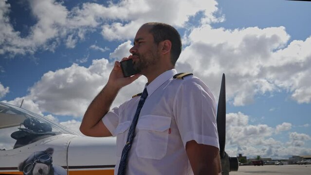 A male pilot speaks at phone near his plane on apron zone