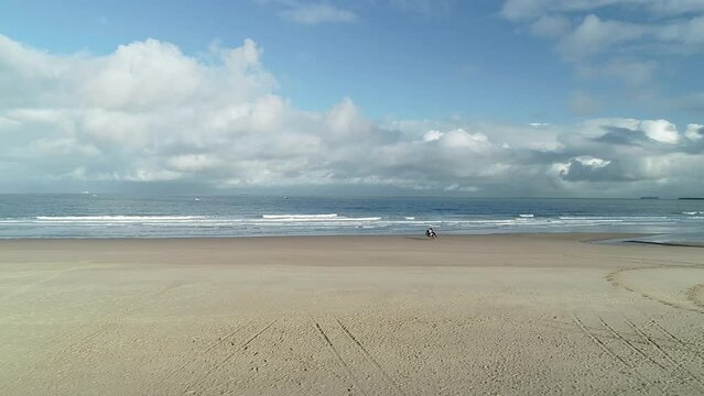 Aerial footage of two people riding horses on a sandy beachin Blankenberge, Belgium