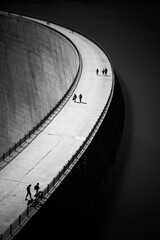 Black and white landscape view of people walking on the Emosson dam