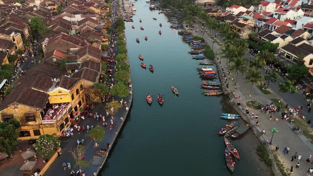 Drone flying at sunset on Hoi An city in Vietnam showcasing river with boats between the buildings