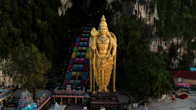 Zoom-out drone shot of the golden statue of Lord Murugan at the Batu Caves Hindu temple.