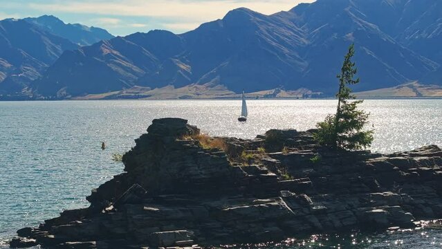 Sailboat framed between rocky edge of small island in Lake Hawea New Zealand