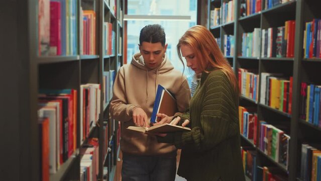 Two students engrossed in book at the library, sharing knowledge and discussion between the shelves of well-stocked library. Education and resource searching concept