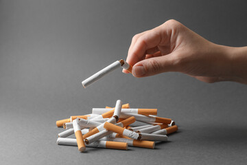 Stop smoking. Woman holding broken cigarette over pile on grey background, closeup