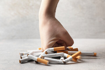 Stop smoking. Woman crushing cigarettes at grey table, closeup