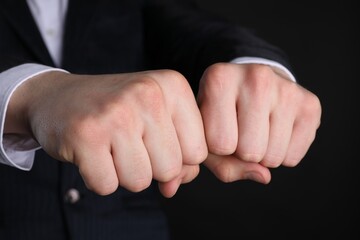Businessman showing fists with space for tattoo on black background, closeup