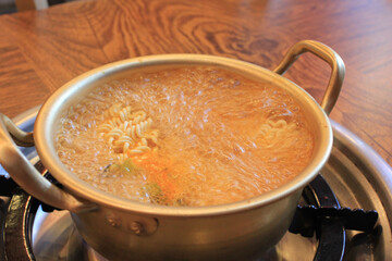 spicy instant noodles are boiling in a metal pot
