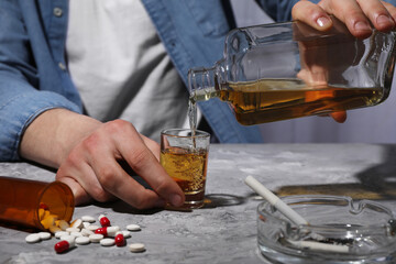 Alcohol and drug addiction. Man pouring whiskey into glass at grey textured table, closeup