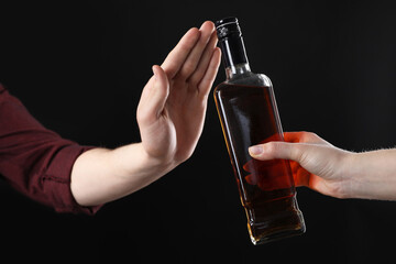 Alcohol addiction. Woman refusing bottle of whiskey on black background, closeup