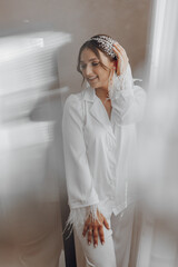 A woman in a white dress is posing for a picture. She is wearing a feather headband and has her hair pulled back. The image has a light and airy feel to it, with the woman's smile
