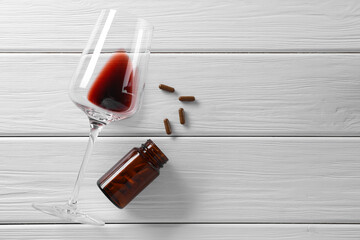 Alcohol and drug addiction. Glass with red wine, bottle and pills on white wooden table, flat lay....