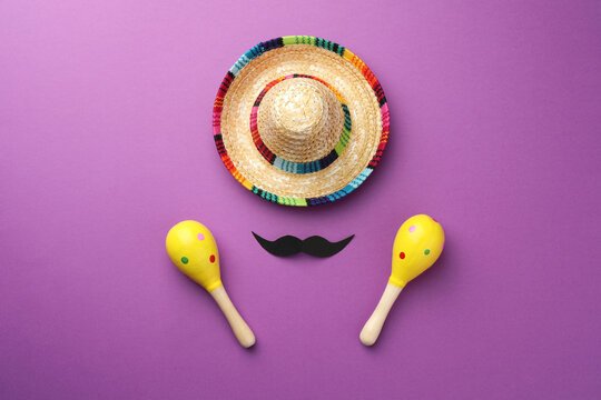 Mexican sombrero hat, fake mustache and maracas on purple background, flat lay