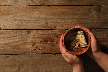 Donate and give concept. Woman holding bowl with coins and dollar banknotes at wooden table, top view. Space for text