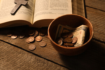 Donate and give concept. Bowl with coins, dollar banknotes, cross and Bible on wooden table, closeup
