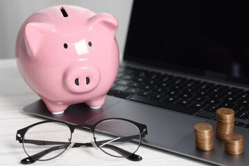 Piggy bank, glasses, coins and laptop on white table