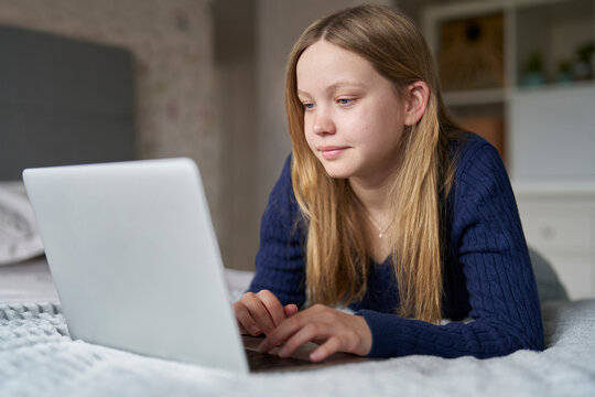 Teenage Girl With Laptop Lying On Bed At Home Gaming, Streaming Film Or Show, Browsing Online Looking At Social Media