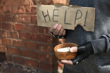 Poor homeless man holding help sign and bowl with donations outdoors, closeup. Space for text