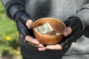 Poor homeless man holding bowl with donations outdoors, closeup