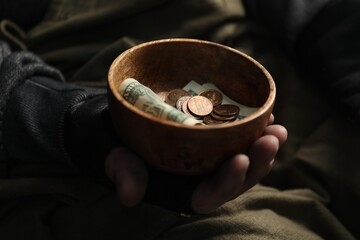 Poor homeless man holding bowl with donations on blurred background, closeup