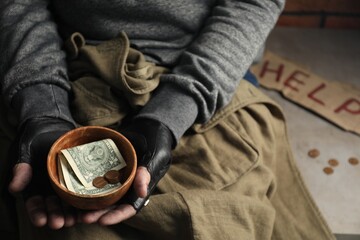 Poor homeless man holding bowl with donations on floor, closeup