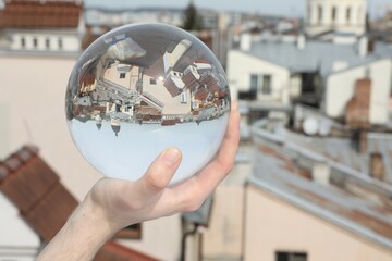 View of beautiful city street, overturned reflection. Man holding crystal ball outdoors, closeup