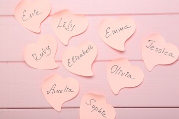 Paper stickers with different names on pink wooden background, flat lay. Choosing baby's name