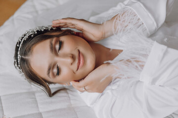 A woman is laying on a bed with her hands on her face. She is wearing a white robe and a headpiece....