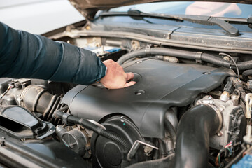 A man opens the plug on a car engine to replace and top up oil, and maintain the car