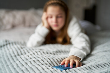 Unhappy Teenage Girl With Mobile Phone Lying On Bed At Home Anxious About Social Media Online...