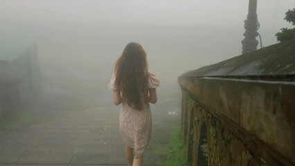 young widow well dressed walking alone  on to cemetery path with blue flower in foggy misty landscape 