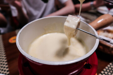 holding a piece of bread dipping in a Swiss style cheese fondue