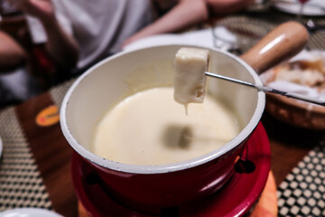 holding a piece of bread dipping in a Swiss style cheese fondue