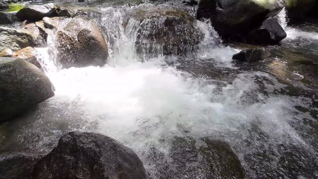 Gentle tracking shot through a picturesque river with majestic waterfall and large stones 4K resolution