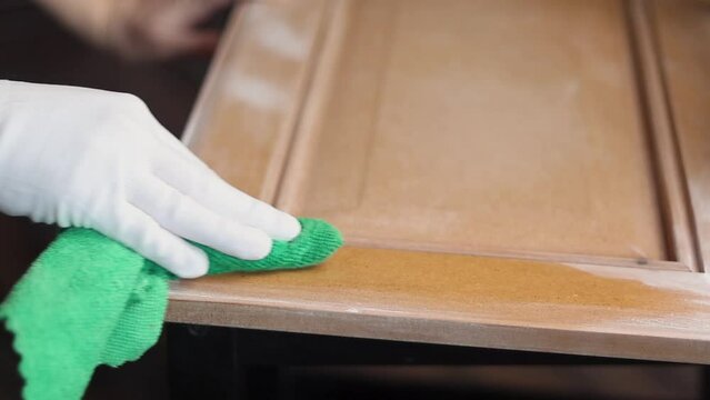Remonier worker in a gloves degreases the surface before painting a wooden product, kitchen facade close up
