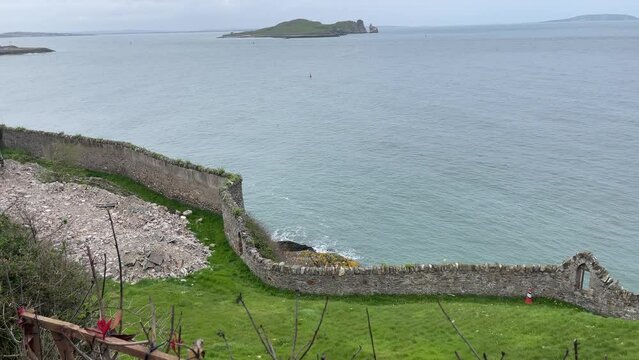 Scenic walking trail along the rugged coastline of Howth, Ireland, leading toward a lighthouse with rocky cliffs, green vegetation, and views of the Irish Sea.