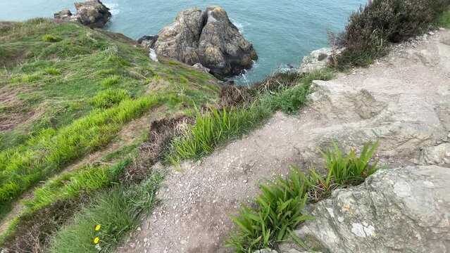 Scenic walking trail along the rugged coastline of Howth, Ireland, leading toward a lighthouse with rocky cliffs, green vegetation, and views of the Irish Sea.