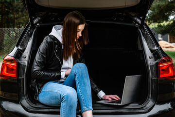 Fototapeta na wymiar Young woman sitting in car trunk with laptop in nature.