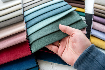 Male hand choosing perfect colorful fabric samples for new sofa and chairs in new home