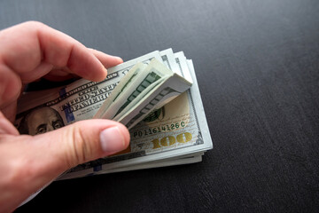 Men's hand holds a pile of american paper dollars on black background