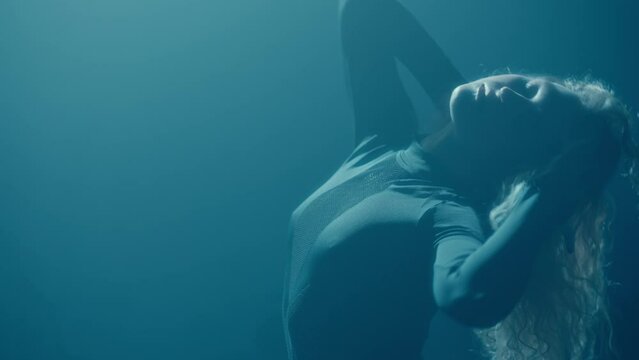 A young woman sensually dances in a dimly lit studio, showcasing her contemporary dance moves in high heels with a passionate and graceful expression in slow motion.