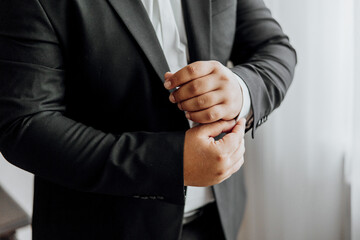 A man in a black suit is getting ready to dress up. He is adjusting his tie and shirt, and his...