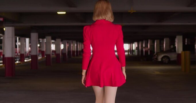 Amidst the concrete confines of a city parking garage, a young Hispanic girl wears a short red dress.