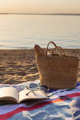 Jute beach bag, wireless headphones, notepad and sunglasses on the striped towel on the sand. Summer vacation lifestyle concept