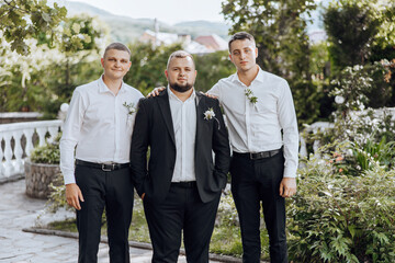 Three men in suits pose for a photo in front of a garden. Scene is formal and elegant, as the men...