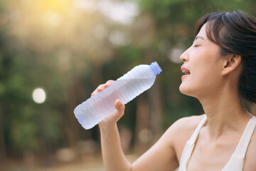 Sportswoman. Fit Asian young woman with white sportswear drinking water after running and enjoying a healthy outdoor. Fitness runner girl in public park. Wellness being concept