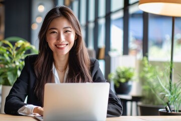 Young asian woman using laptop in modern office interiors.