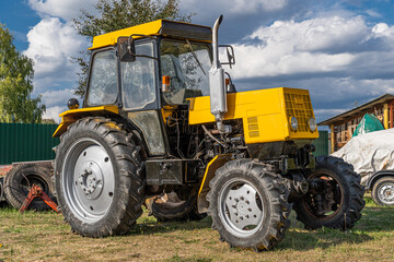 Wheeled Russian diesel tractor of yellow and black color on a sunny day stands on the ground with...