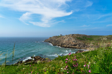 L'été à la Pointe du Millier : parterre de fleurs champêtres, eaux turquoises de la mer d'Iroise et maison phare sur sa pointe rocheuse, une scène emblématique de la Bretagne.